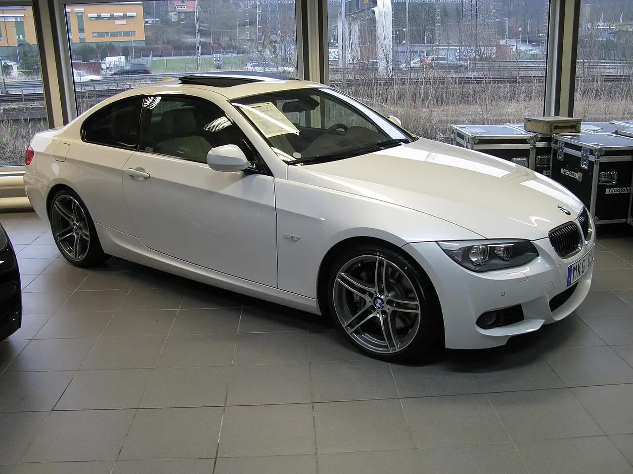 White BMW 335i M Sport Coupe (E92 LCI), front three-quarter view in a showroom
