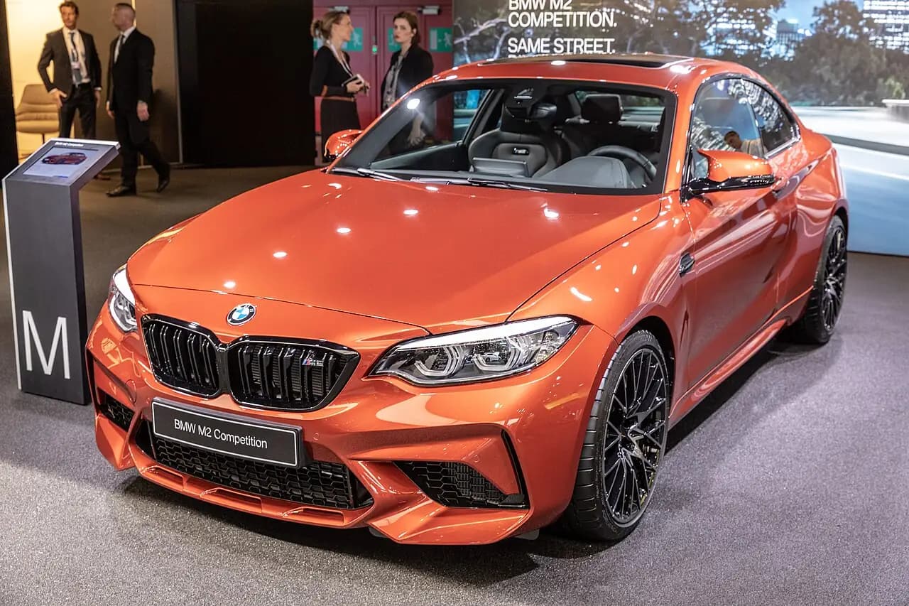 Orange 2019 BMW M2 Competition (F87) coupe on a motor show stand, front three-quarter view
